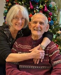 Two people embrace, with Christmas tree decorations in the background